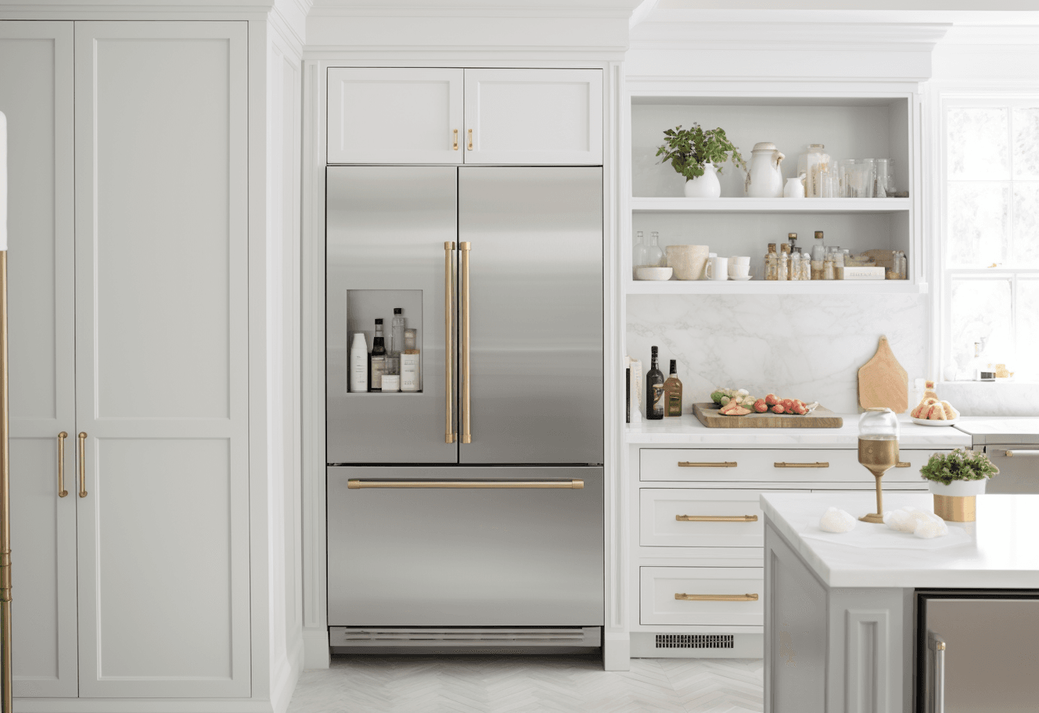 A stainless steel French door fridge freezer fitted between white kitchen cabinets